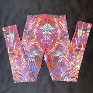May include: Vibrant leggings with a colorful abstract design. The leggings feature a mix of purple, pink, orange, and white patterns. The design is symmetrical and covers the entire surface of the leggings.