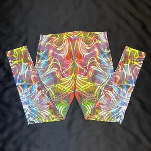 May include: Vibrant leggings with a colorful abstract design. The leggings feature a mix of neon yellow, purple, orange, and blue lines and shapes. The leggings are made of a stretchy material and are folded on a black surface.