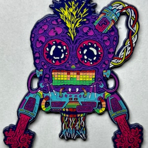 May include: A vibrant, stylized enamel pin featuring a purple, skull-like figure with large eyes and a rainbow-colored mouth. The design includes intricate details, with yellow, blue, and red accents, and a unique, flowing design emanating from the bottom.