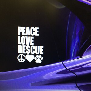 May include: White decal with the words "PEACE LOVE RESCUE" in a stacked format, accompanied by a peace sign, a heart, and a paw print. The background is a dark, abstract design with shades of purple and blue.