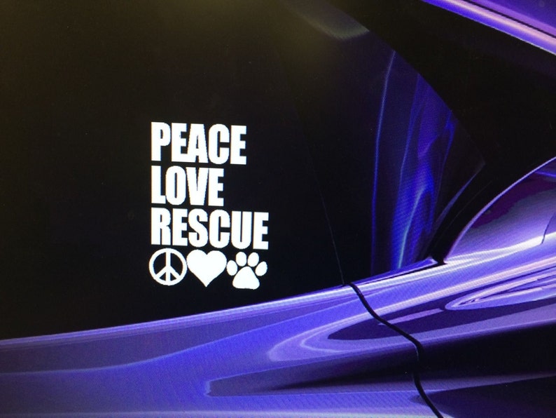 May include: White decal with the words "PEACE LOVE RESCUE" in a stacked format, accompanied by a peace sign, a heart, and a paw print. The background is a dark, abstract design with shades of purple and blue.