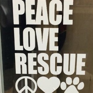 May include: White text on a dark background reads "PEACE LOVE RESCUE" with a peace symbol, heart, and paw print below. The image is likely a decal or sticker, promoting animal rescue and a message of peace and love.