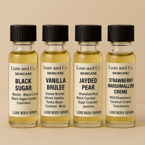 May include: Four small glass bottles of Luxe and Co. skincare body serum with black caps. The labels read "Black Sugar", "Vanilla Brulee", "Jayded Pear", and "Strawberry Marshmallow Creme". Each bottle contains a golden liquid.