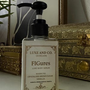 May include: A clear glass bottle of Luxe and Co. skincare serum with a black pump. The label reads "FIGures Luxe Body Serum" with "Warm Fig, Crystalized Brown Sugar, Vanilla" ingredients. The bottle is displayed in front of a decorative background.