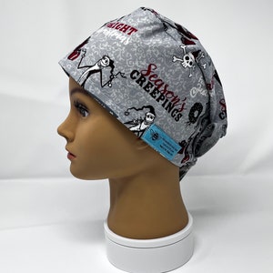 May include: A gray surgical scrub cap featuring a pattern of Jack Skellington and other characters from The Nightmare Before Christmas. The cap has the words "Season's Creepings" and "Nightmare Before Christmas" printed on it. The cap is made of a soft, breathable fabric.