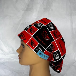 May include: A patterned scrub cap featuring the Oregon State University logo in black and white on a red background. The cap is worn by a mannequin head. The text "Oregon State" is visible on the cap.