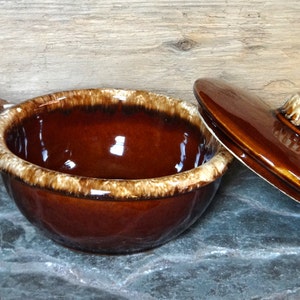 May include: A brown and white glazed ceramic soup bowl with a handle and lid. The bowl has a brown glaze with white streaks and the lid has a brown glaze with a white knob.