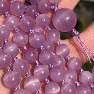 May include: Close-up of a lavender-colored beaded necklace. The beads are round and strung together with matching lavender-colored cord. The beads have a smooth, polished surface and vary slightly in size.