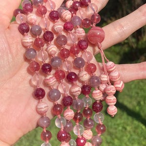 May include: A multi-strand beaded necklace with pink, red, and clear beads. The beads are made of various materials, including crystal, agate, and quartz.