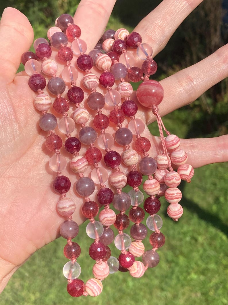 May include: A multi-strand beaded necklace with pink, red, and clear beads. The beads are made of various materials, including crystal, agate, and quartz.
