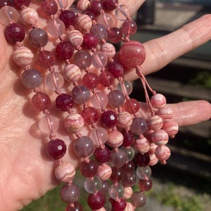May include: A multi-strand necklace made of pink, white, and clear beads. The beads are round and have a smooth, polished finish. The necklace is strung on a thin, white cord.