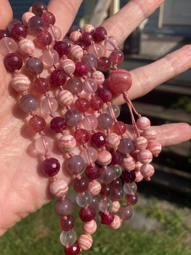 May include: A multi-strand necklace made of pink, white, and clear beads. The beads are round and have a smooth, polished finish. The necklace is strung on a thin, white cord.