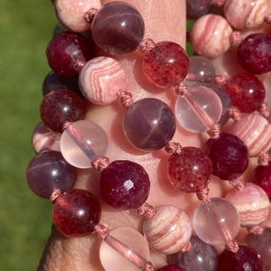 May include: A close-up of a multi-strand beaded necklace with pink, red, and clear beads. The beads are made of various materials, including gemstone and glass.