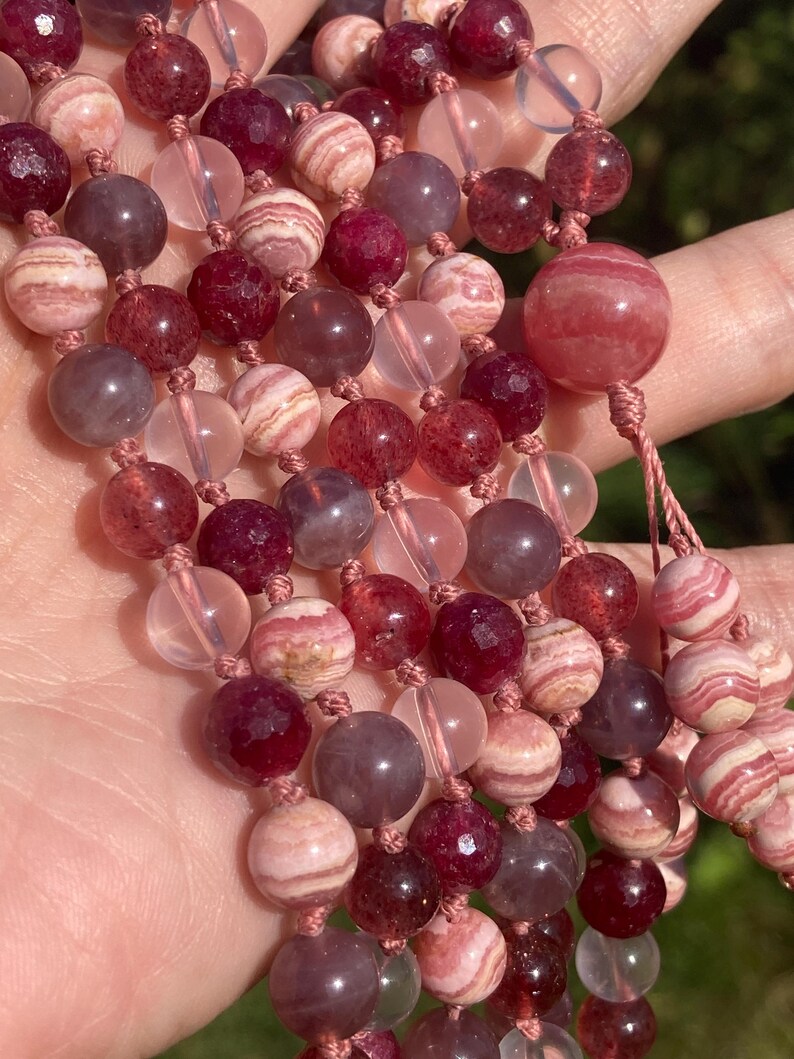 May include: A multi-strand necklace made of pink, red, and clear beads. The beads are round and have a smooth, polished finish. The necklace is strung on a thin, pink cord.