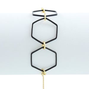 May include: A black and gold geometric bracelet with three hexagon shapes connected by gold rings. The bracelet has a gold chain extension.