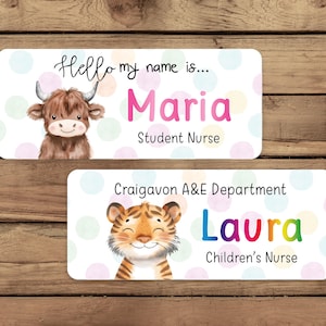 Op de afbeelding: Twee witte naamstickers met kleurrijke stippen. De bovenste sticker heeft een cartoon hooglandkoe en de tekst "Hello my name is... Maria Student Nurse". De onderste sticker heeft een cartoon tijger en de tekst "Craigavon A&E Department Laura Children's Nurse".