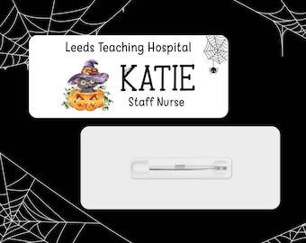 May include: A white name tag with a black spider web design and a black cat wearing a witch's hat sitting in a jack-o'-lantern. The text on the tag reads "Leeds Teaching Hospital", "KATIE", and "Staff Nurse".