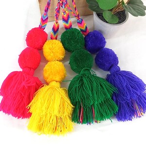 May include: Five colorful pom-pom keychains with rainbow striped cords. The pom-poms are pink, yellow, green, and blue.