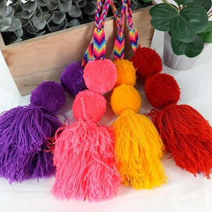May include: Five colorful pom-pom tassels with rainbow striped cords. The tassels are purple, pink, yellow, and red.