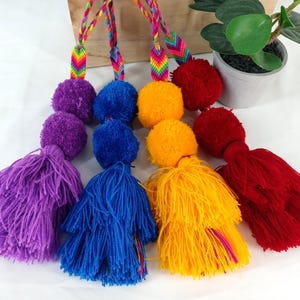May include: Four colorful pom-pom tassels with rainbow striped cords. The tassels are purple, blue, yellow, and red.