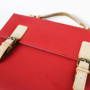 May include: A red leather satchel with white leather straps and buckles. The bag has a top handle.