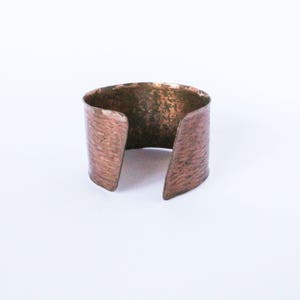 Peut inclure: Un bracelet en cuivre martelé avec une finition rustique. Le bracelet est ouvert aux deux extrémités et a une forme légèrement incurvée.
