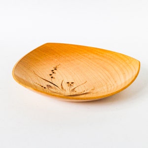 Könnte beinhalten: Eine kleine, quadratische Holzschale mit hellbrauner Oberfläche. Die Schale hat ein zartes, eingebranntes Blumenmuster.