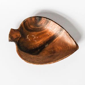 Könnte beinhalten: Eine dunkelbraune Holzschale in Blattform mit einem Griff. Die Schale ist aus Naturholz gefertigt und hat einen rustikalen Look.