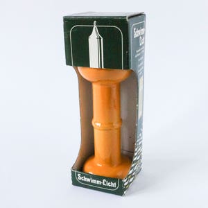 Könnte beinhalten: Ein orangefarbener Kerzenhalter aus Keramik in einer Schachtel mit dem Text "Schwimm-Licht" auf der Vorderseite.