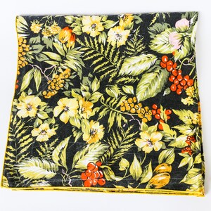 Könnte beinhalten: Ein schwarzer Stoff mit einem floralen Muster mit gelben Blumen, grünen Blättern und roten Beeren. Der Stoff hat einen gelben Rand.