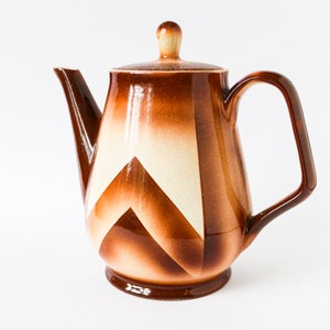 Könnte beinhalten: Eine braune Teekanne aus Keramik mit geometrischem Muster. Die Teekanne hat einen weißen Deckel und einen braunen Henkel.