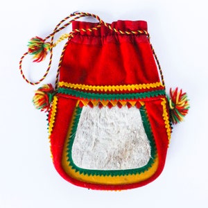 Könnte beinhalten: Eine rote, grüne und gelbe Kordeltasche mit einer weißen Fellklappe. Die Tasche hat einen dekorativen Besatz und Quasten.
