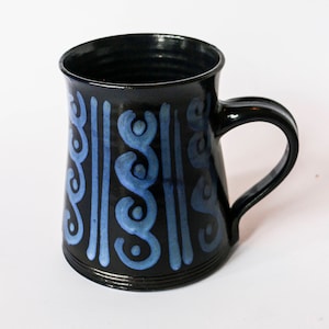 May include: A black ceramic mug with a blue and white geometric pattern. The mug has a wide base and a rounded handle.