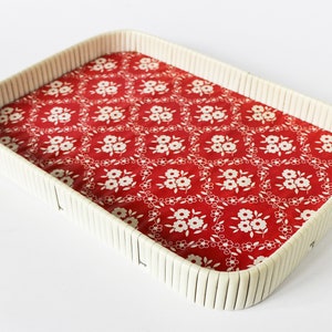 Puede incluir: Una bandeja de mimbre blanca con un patrón floral rojo y blanco. La bandeja es perfecta para servir aperitivos o bebidas.