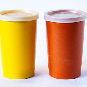 May include: Two plastic cups with lids. The cup on the left is yellow and the cup on the right is orange.