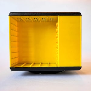 May include: A yellow plastic storage container with a black top and base. The container features internal slots and dividers, ideal for organisation. The design is rectangular with a rotating base. The container is likely for small items.
