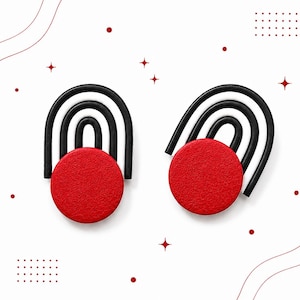 Puede incluir: Un par de pendientes con una base circular roja sólida y tres líneas arqueadas negras que se extienden hacia arriba. El diseño es simétrico, con los círculos rojos colocados en la parte inferior y los arcos negros formando una figura de arcoíris sobre cada círculo, sobre un fondo blanco con pequeños puntos rojos y estrellas.