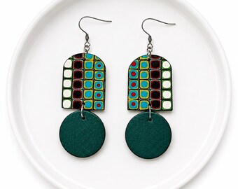 May include: A pair of handcrafted earrings with a geometric design. Each earring features a dark green circular pendant suspended below a colorful arch-shaped top. The arch has a pattern of squares in teal, red, black, and white.