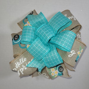 May include: A turquoise and beige bow with a checkered pattern and a blue truck with flowers printed on the fabric. The bow has the text "Hello Spring" printed on it.
