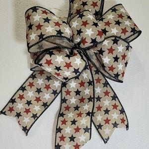 May include: A brown, white, and red star patterned ribbon bow with black trim. The bow is tied in a loop with two tails.