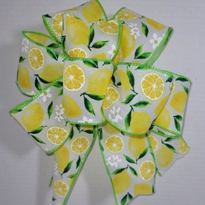 May include: A white ribbon with a green edge features a lemon print with yellow lemons, green leaves, and white flowers.
