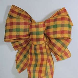 May include: A large, multi-colored plaid bow with a yellow, green, and red checkered pattern. The bow is made of fabric and has a rustic, farmhouse style.