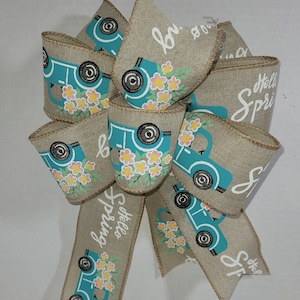 May include: A burlap bow with a blue truck design and floral accents. The bow has the text "Hello Spring" written on it.