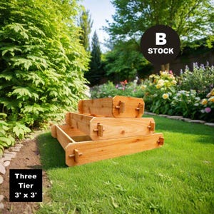 May include: Three-tier wooden raised garden bed in a backyard setting. The bed is made of natural cedar wood and measures 3 feet by 3 feet. The bed is in stock.