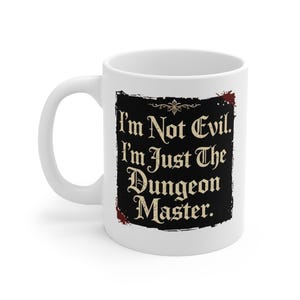 May include: White ceramic mug featuring the text "I'm Not Evil. I'm Just The Dungeon Master." in a black frame. The mug has a curved handle and is suitable for hot or cold drinks. The design includes decorative elements.