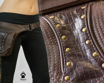 Könnte beinhalten: Ein brauner Ledergürtel mit einer großen, dekorativen Tasche. Die Tasche hat einen Reißverschluss und ist mit Metallnieten verziert. Der Gürtel wird über einer schwarzen Hose getragen.