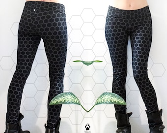 Könnte beinhalten: Schwarze Leggings mit einem Wabenmuster. Die Leggings werden von einer Person mit einem Tattoo auf dem unteren Rücken getragen. Die Person steht vor einer weißen gekachelten Wand mit einer grünen Pflanze im Vordergrund.