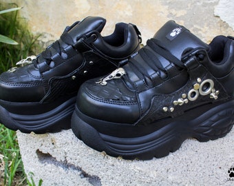 Könnte beinhalten: Schwarze Plateausneaker mit silbernen Akzenten und einem strukturierten Lederdesign. Die Schuhe haben eine dicke Plateau-Sohle und einen Schnürverschluss.