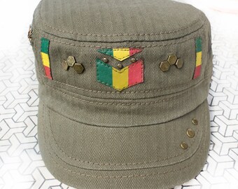 Könnte beinhalten: Eine grüne Militärkappe mit einem roten, gelben und grünen Patch auf der Vorderseite. Der Patch hat ein Design, das an eine Flagge erinnert. Die Kappe hat einen Schirm und ist mit Metallverzierungen verziert.