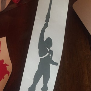 May include: A gray silhouette of a figure holding a sword raised high above their head.